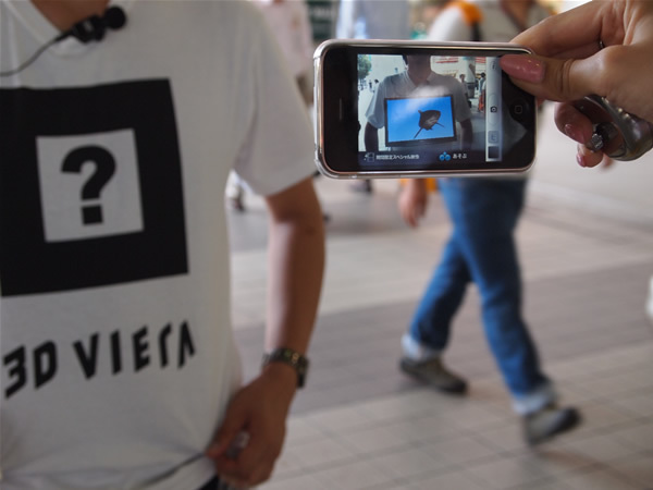 Tシャツに表示された「？」を、専用iPhoneアプリのカメラを通じて見るとさまざまな動物が映し出される。写真はサメが写っているところ